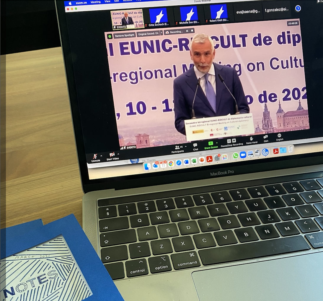 A laptopscreen, showing Stefano Sannino standing at a podium and speaking into a micophone.